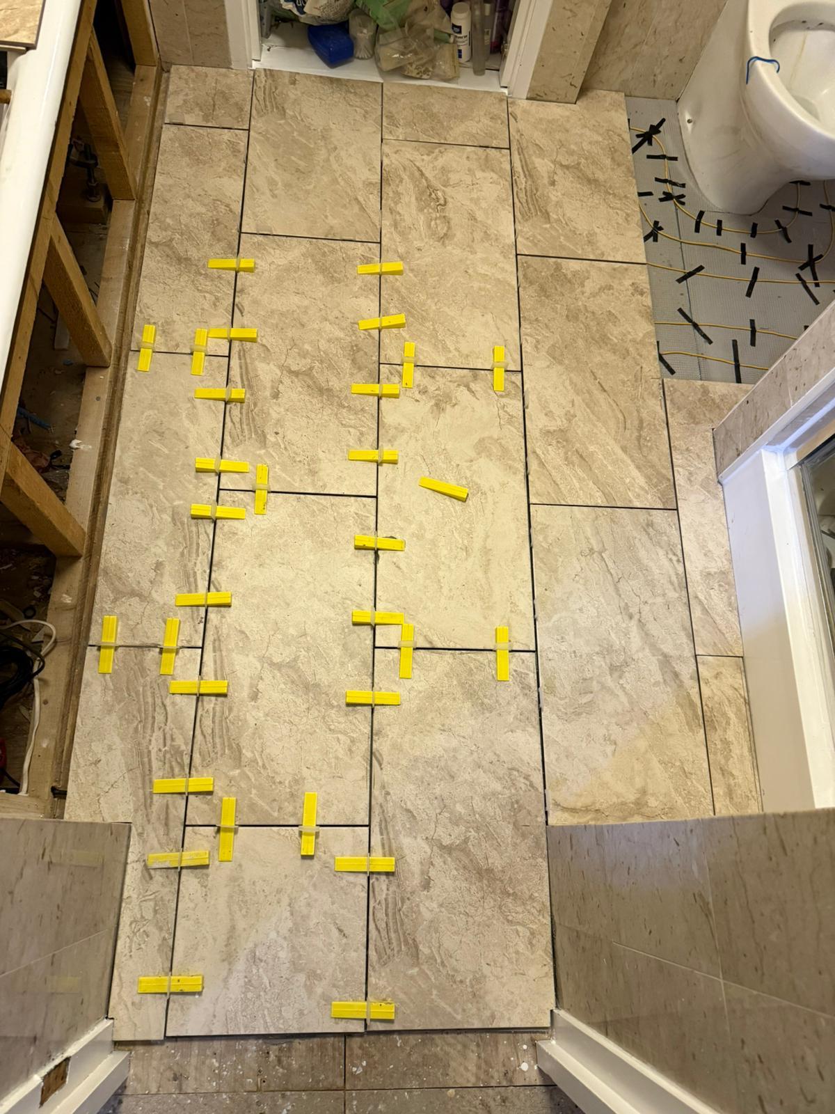 Bathroom floor tiling progress with tile spacers and levelling clips