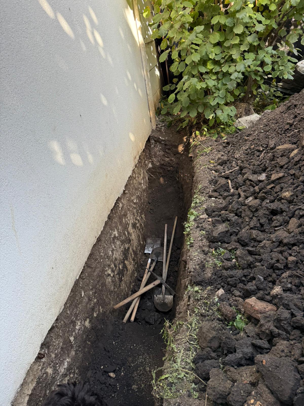 Trench being dug by hand along the base of the wall to expose the foundation